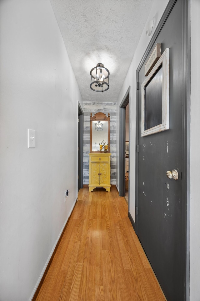 corridor with a notable chandelier, light hardwood / wood-style floors, and a textured ceiling