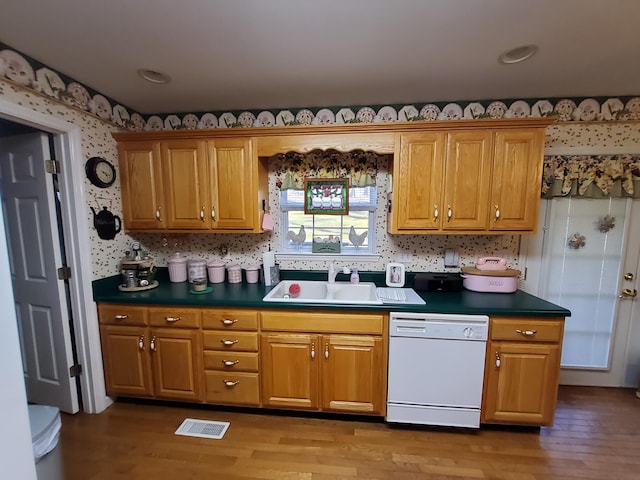 kitchen with dark countertops, brown cabinets, dishwasher, and a sink