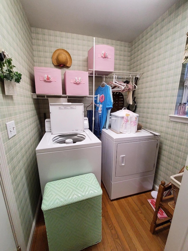 laundry area with laundry area, washing machine and dryer, wallpapered walls, and wood finished floors