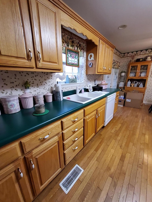 kitchen with dishwasher, dark countertops, a sink, and visible vents