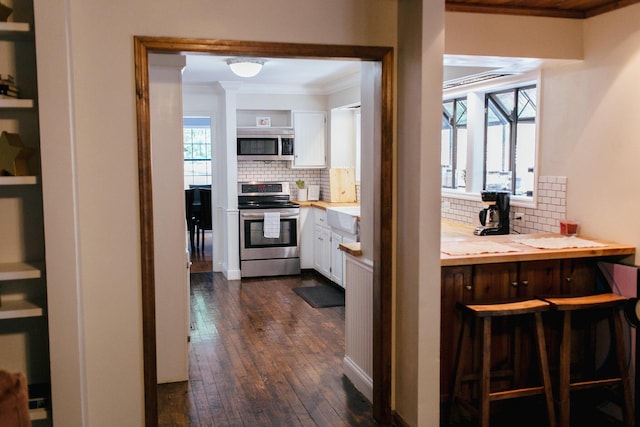 kitchen with backsplash, white cabinets, crown molding, dark hardwood / wood-style flooring, and stainless steel appliances