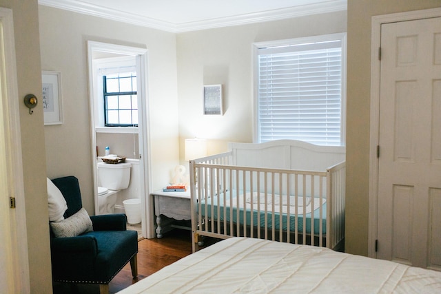 bedroom featuring hardwood / wood-style flooring, a crib, crown molding, and ensuite bath