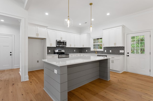 kitchen with appliances with stainless steel finishes, light wood-type flooring, a wealth of natural light, white cabinets, and a center island