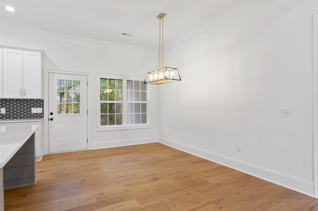 unfurnished dining area featuring light hardwood / wood-style flooring, ornamental molding, and a notable chandelier