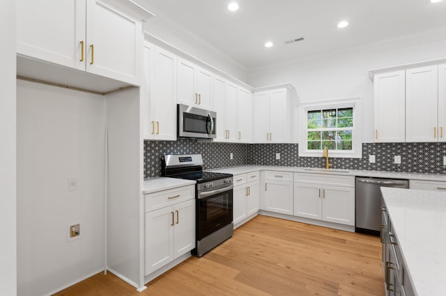 kitchen featuring white cabinets, sink, tasteful backsplash, light hardwood / wood-style floors, and stainless steel appliances