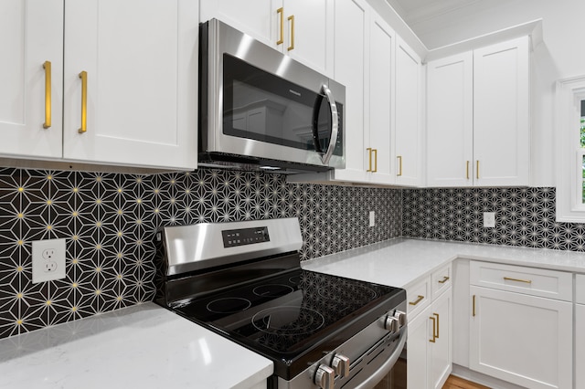 kitchen featuring appliances with stainless steel finishes, backsplash, white cabinetry, and light stone counters