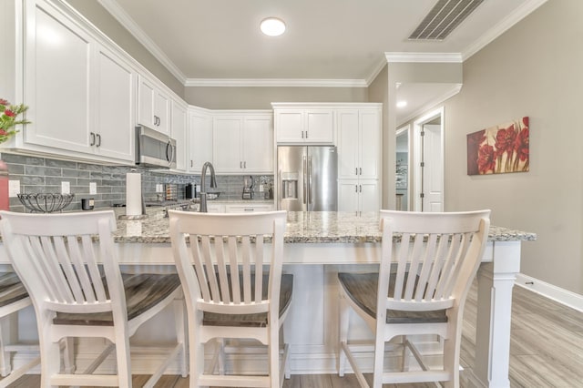 kitchen with light stone countertops, appliances with stainless steel finishes, a breakfast bar, and white cabinets