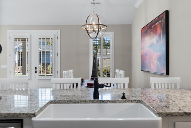 kitchen featuring sink, an inviting chandelier, hanging light fixtures, light stone countertops, and french doors