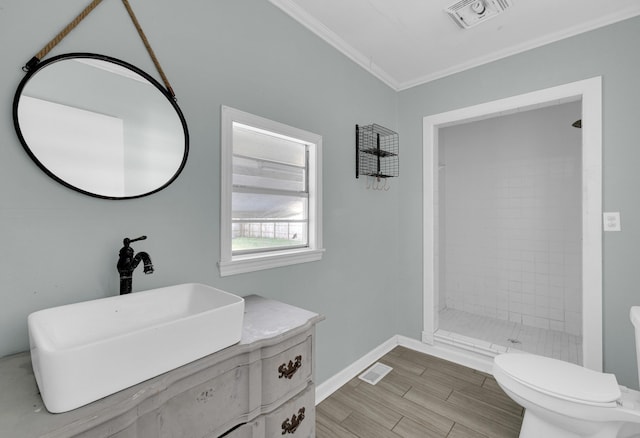 bathroom featuring a tile shower, vanity, toilet, and ornamental molding