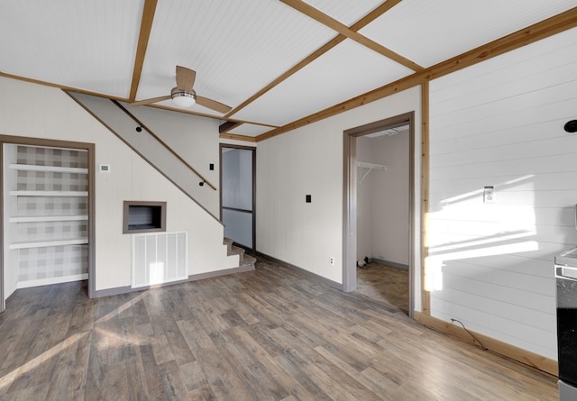 unfurnished living room featuring beam ceiling, ceiling fan, dark wood-type flooring, and wood walls