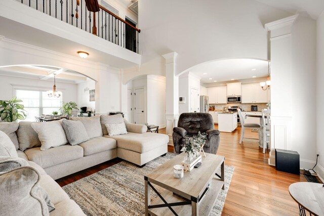 living room featuring light hardwood / wood-style flooring, ornamental molding, a high ceiling, and an inviting chandelier