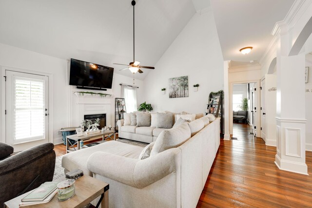 living room with dark wood-type flooring, high vaulted ceiling, crown molding, ceiling fan, and ornate columns