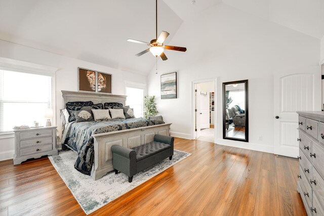 bedroom featuring ceiling fan, light hardwood / wood-style flooring, high vaulted ceiling, and multiple windows