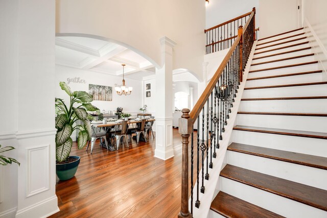 stairs featuring beamed ceiling, wood-type flooring, coffered ceiling, and an inviting chandelier