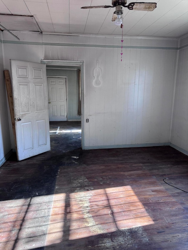 spare room featuring wooden walls, ceiling fan, and dark wood-type flooring