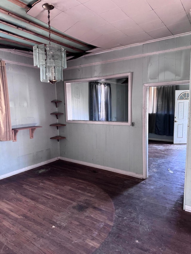 unfurnished room featuring dark hardwood / wood-style flooring, an inviting chandelier, and wood walls