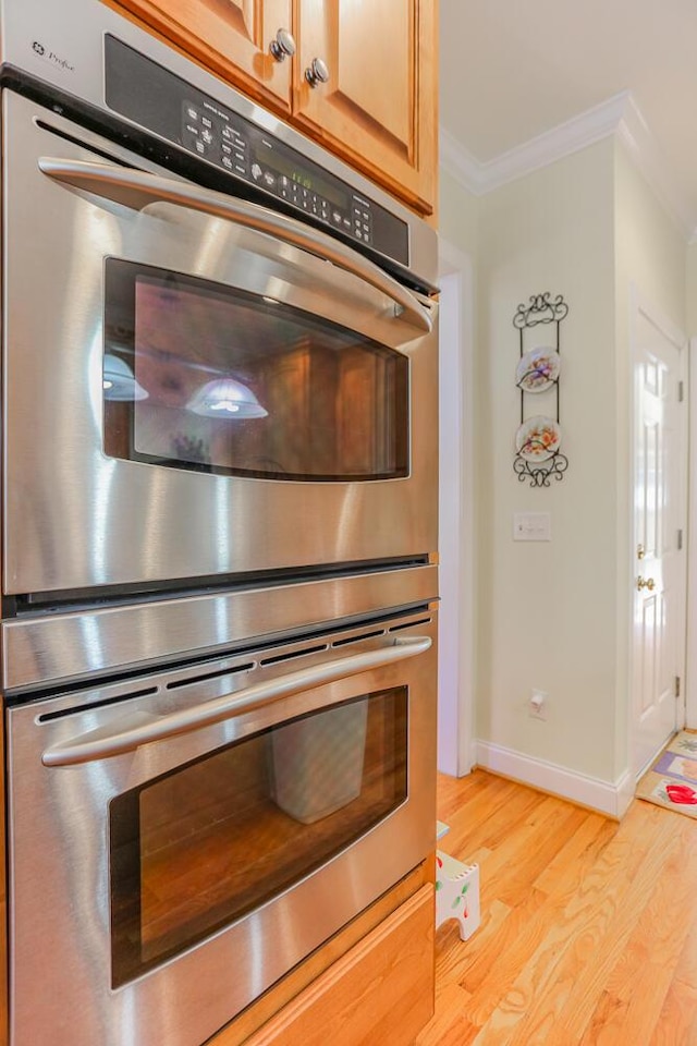 room details with double oven, light brown cabinetry, crown molding, and light hardwood / wood-style flooring