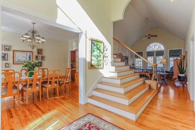 staircase with high vaulted ceiling, wood-type flooring, ceiling fan with notable chandelier, and ornamental molding