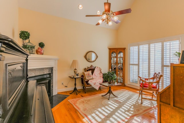 living area featuring light hardwood / wood-style floors, high vaulted ceiling, ceiling fan, and a premium fireplace