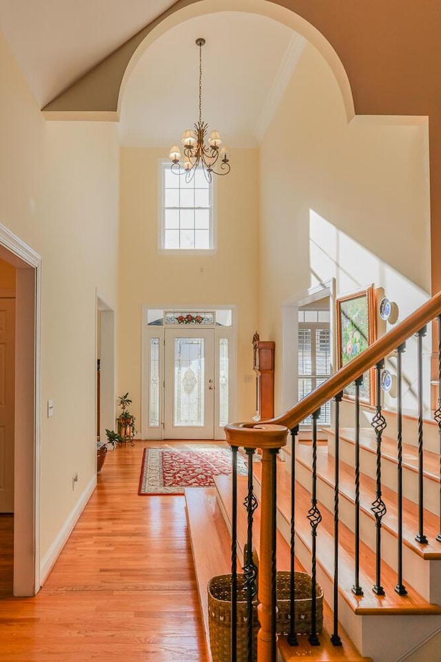 foyer with a towering ceiling, an inviting chandelier, ornamental molding, and light wood-type flooring