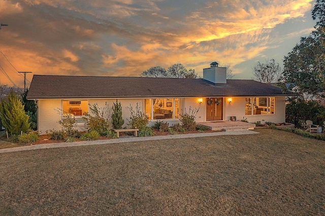 single story home featuring a yard, brick siding, and a chimney