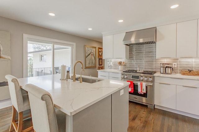 kitchen with dark wood-type flooring, sink, wall chimney range hood, range with two ovens, and white cabinetry