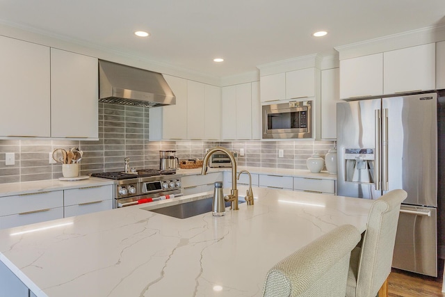 kitchen with light stone countertops, appliances with stainless steel finishes, wall chimney exhaust hood, and sink