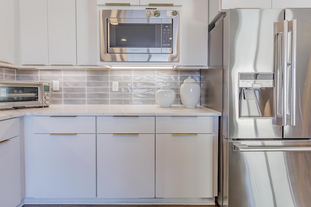 kitchen with white cabinets, backsplash, stainless steel appliances, and light stone counters