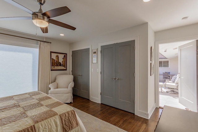 bedroom with multiple windows, dark hardwood / wood-style flooring, two closets, and ceiling fan