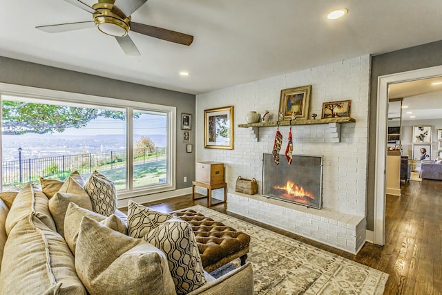 living room featuring dark hardwood / wood-style flooring, a brick fireplace, and ceiling fan