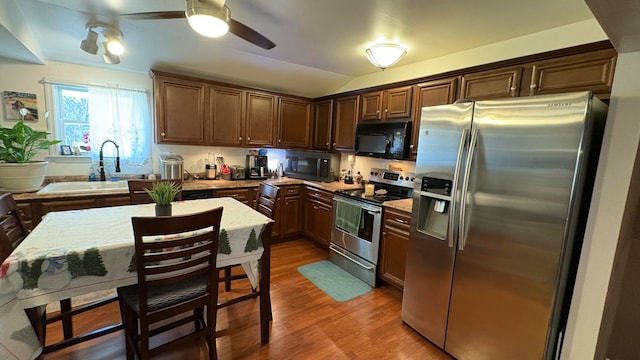 kitchen with sink, vaulted ceiling, appliances with stainless steel finishes, a kitchen island, and dark hardwood / wood-style flooring