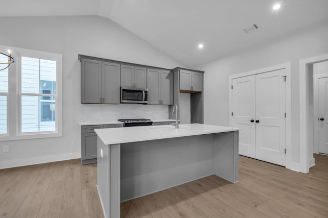 kitchen with lofted ceiling, a center island with sink, sink, light hardwood / wood-style flooring, and gray cabinets