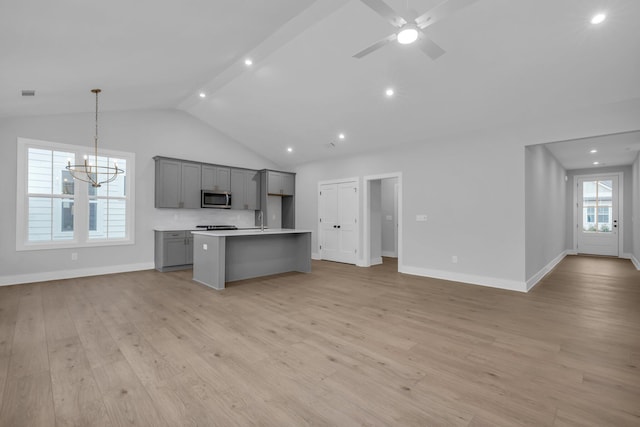 kitchen with gray cabinetry, light hardwood / wood-style flooring, lofted ceiling with beams, decorative light fixtures, and a center island with sink