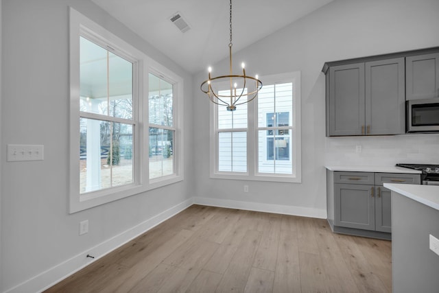 unfurnished dining area with a notable chandelier, vaulted ceiling, and light wood-type flooring