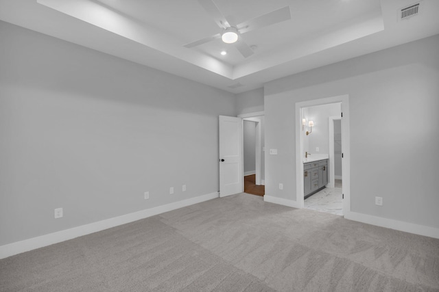 unfurnished bedroom featuring ceiling fan, light colored carpet, connected bathroom, and a tray ceiling