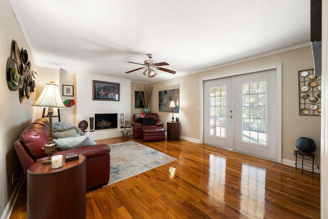 living room with hardwood / wood-style floors, french doors, ceiling fan, ornamental molding, and a fireplace