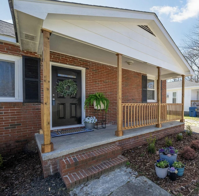 doorway to property featuring covered porch and brick siding