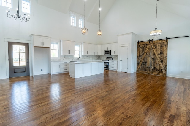 kitchen with dark wood-type flooring, high vaulted ceiling, a barn door, white cabinetry, and stainless steel appliances