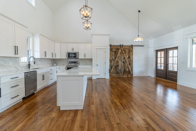 kitchen featuring pendant lighting, a barn door, high vaulted ceiling, and appliances with stainless steel finishes