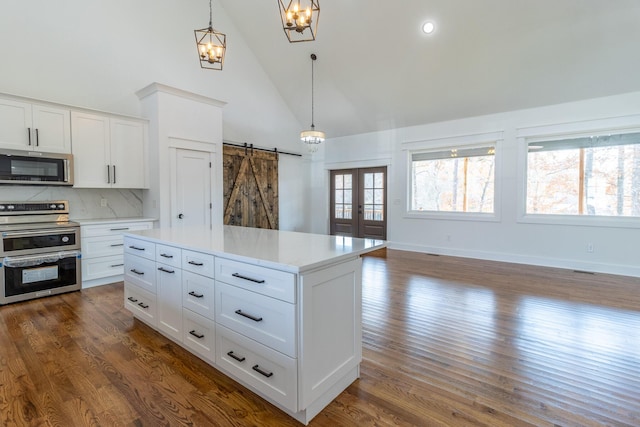 kitchen with stainless steel appliances, dark wood-type flooring, a barn door, decorative light fixtures, and white cabinets