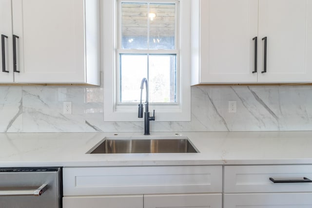 kitchen featuring white cabinets, backsplash, light stone counters, and sink