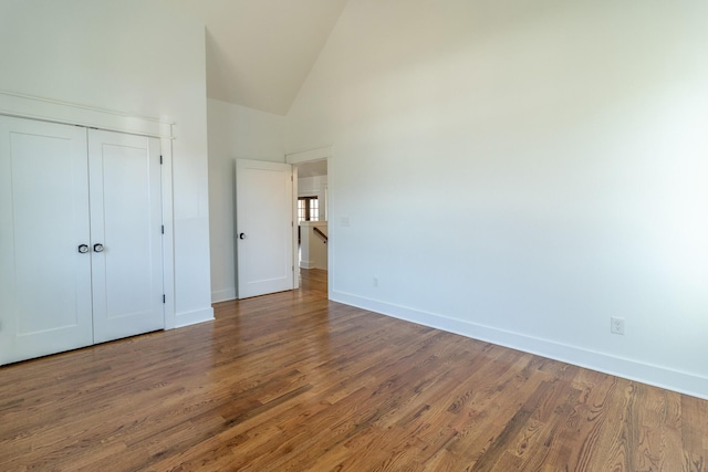 unfurnished bedroom featuring wood-type flooring, high vaulted ceiling, and a closet