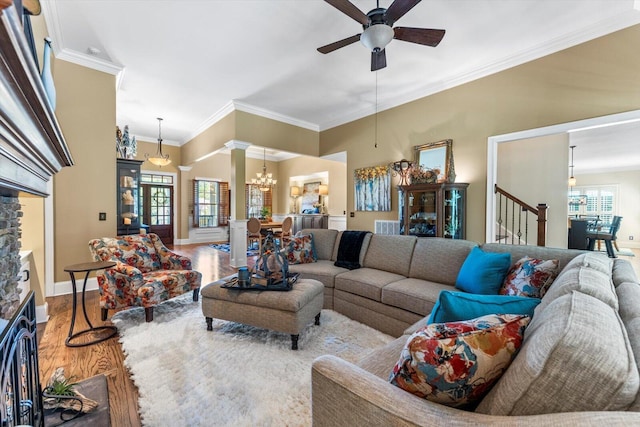 living room with ornate columns, ceiling fan with notable chandelier, a fireplace, hardwood / wood-style flooring, and crown molding