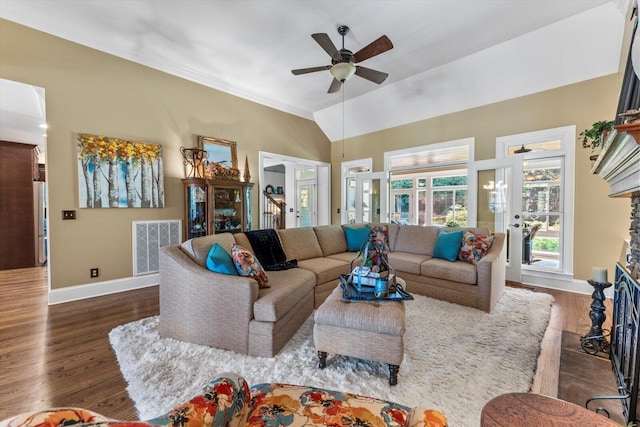 living room with a stone fireplace, dark wood-type flooring, ceiling fan, and vaulted ceiling