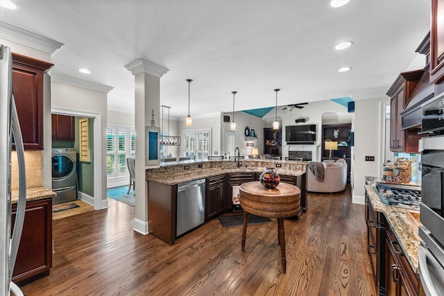 kitchen featuring appliances with stainless steel finishes, dark hardwood / wood-style flooring, washer / clothes dryer, a stone fireplace, and decorative light fixtures