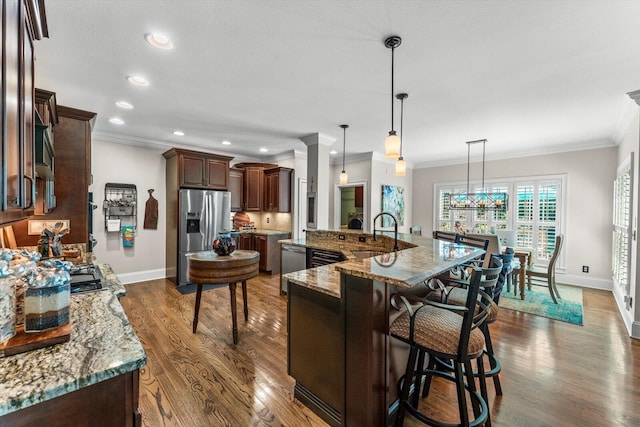 kitchen featuring pendant lighting, crown molding, light stone countertops, and appliances with stainless steel finishes