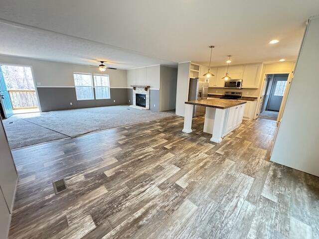 kitchen featuring decorative light fixtures, a center island, stainless steel appliances, hardwood / wood-style floors, and white cabinets