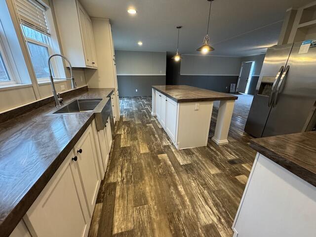 kitchen with dark wood-type flooring, white cabinetry, stainless steel fridge with ice dispenser, a kitchen island, and pendant lighting