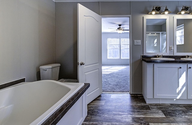 bathroom with hardwood / wood-style flooring, ceiling fan, vanity, toilet, and a bathing tub