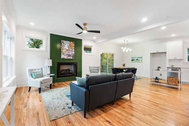 living room with ceiling fan with notable chandelier, a large fireplace, light hardwood / wood-style floors, and ornamental molding